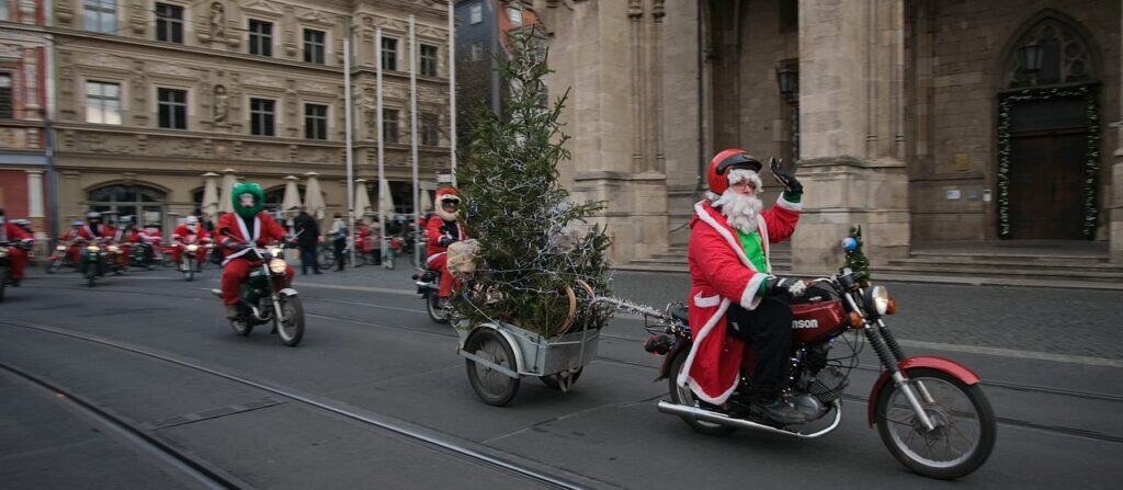 Weihnachtsmann auf Motorrad mit aufrecht stehendem Tannenbaum in einem Anhänger der Stadt.